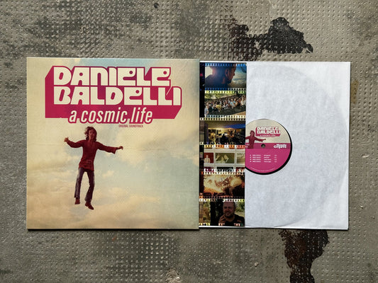 Funda e interior del vinilo Daniele Baldelli – A Cosmic Life (Original Soundtrack), LP de Mondo Groove con insert fotográfico y etiqueta central rosa con pistas visibles.