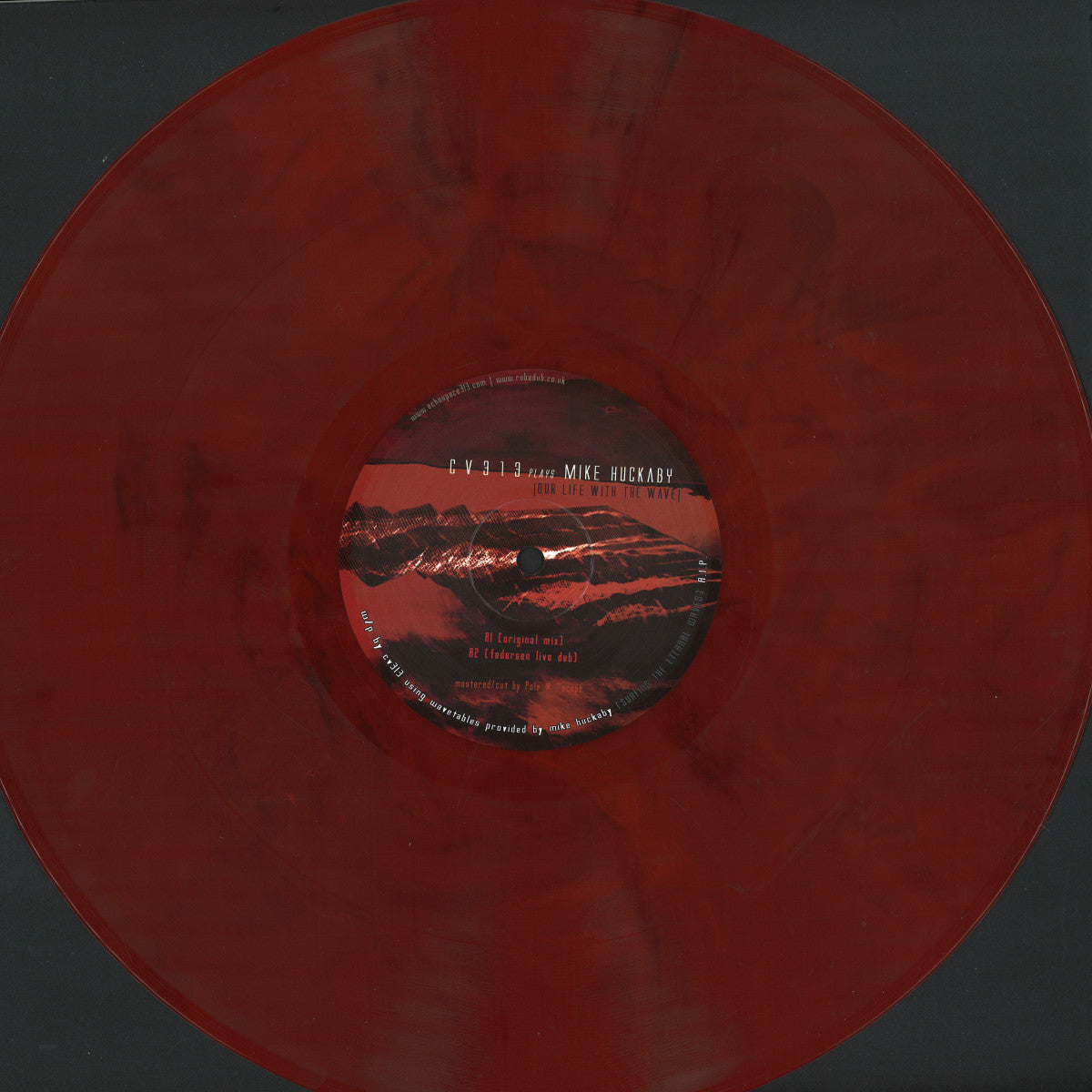 Vista frontal completa del vinilo rojo jaspeado cv313 Plays Mike Huckaby – Our Life With The Wave con la etiqueta del lado A centrada sobre fondo negro.