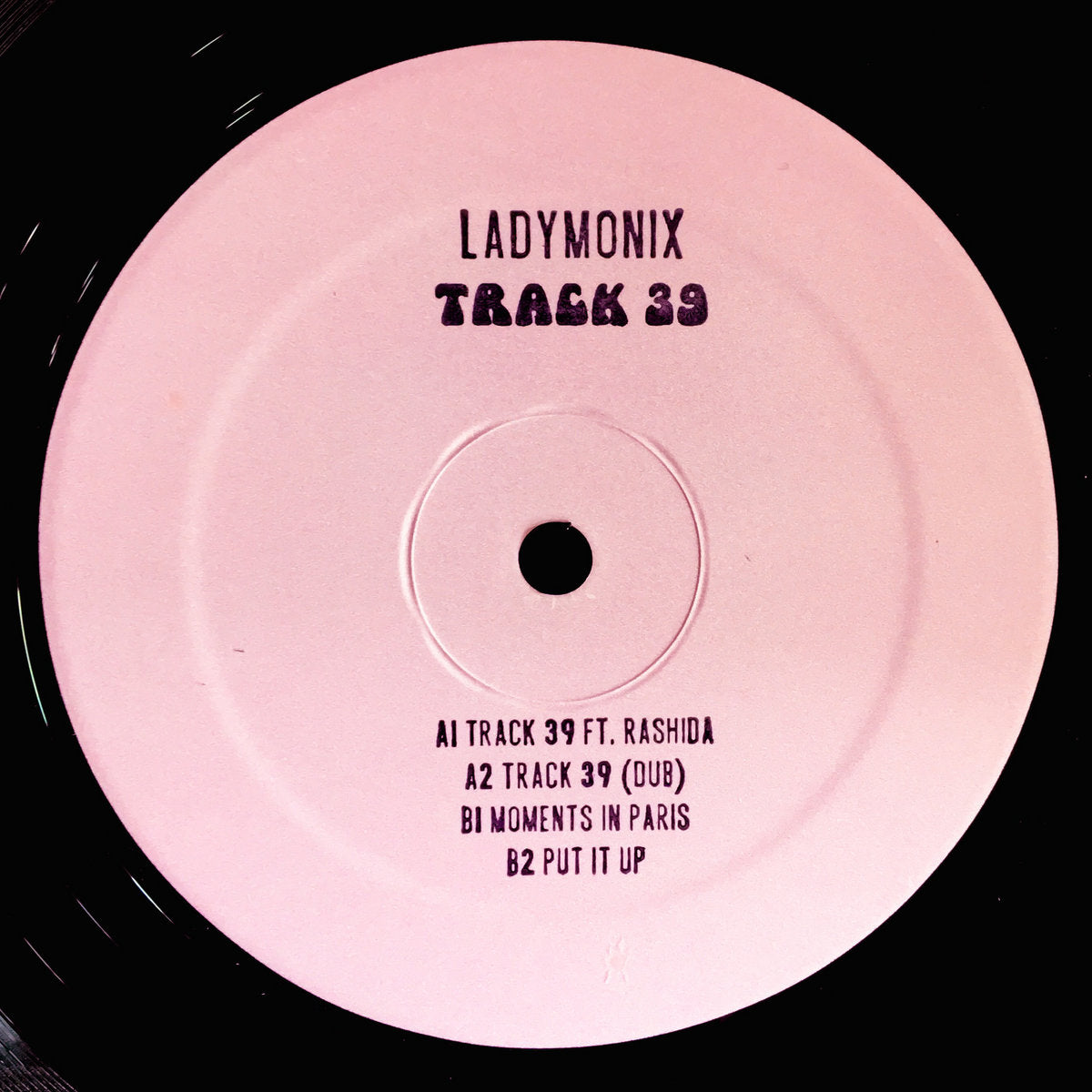 Portada delantera del vinilo LADYMONIX - "Track 39" publicado por Frizner Electric en formato 12". Diseño minimalista con fondo rosa y tipografía negra. Tracklist impreso con los temas del disco.