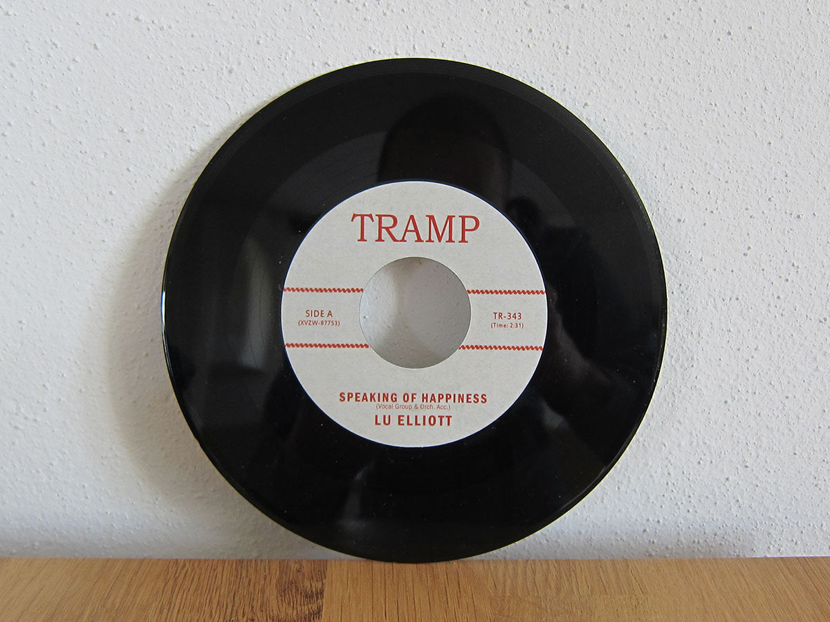 Vinilo de 7 pulgadas Lu Elliott – Speaking Of Happiness de Tramp Records apoyado en la pared, mostrando el lado A con su distintiva etiqueta central.